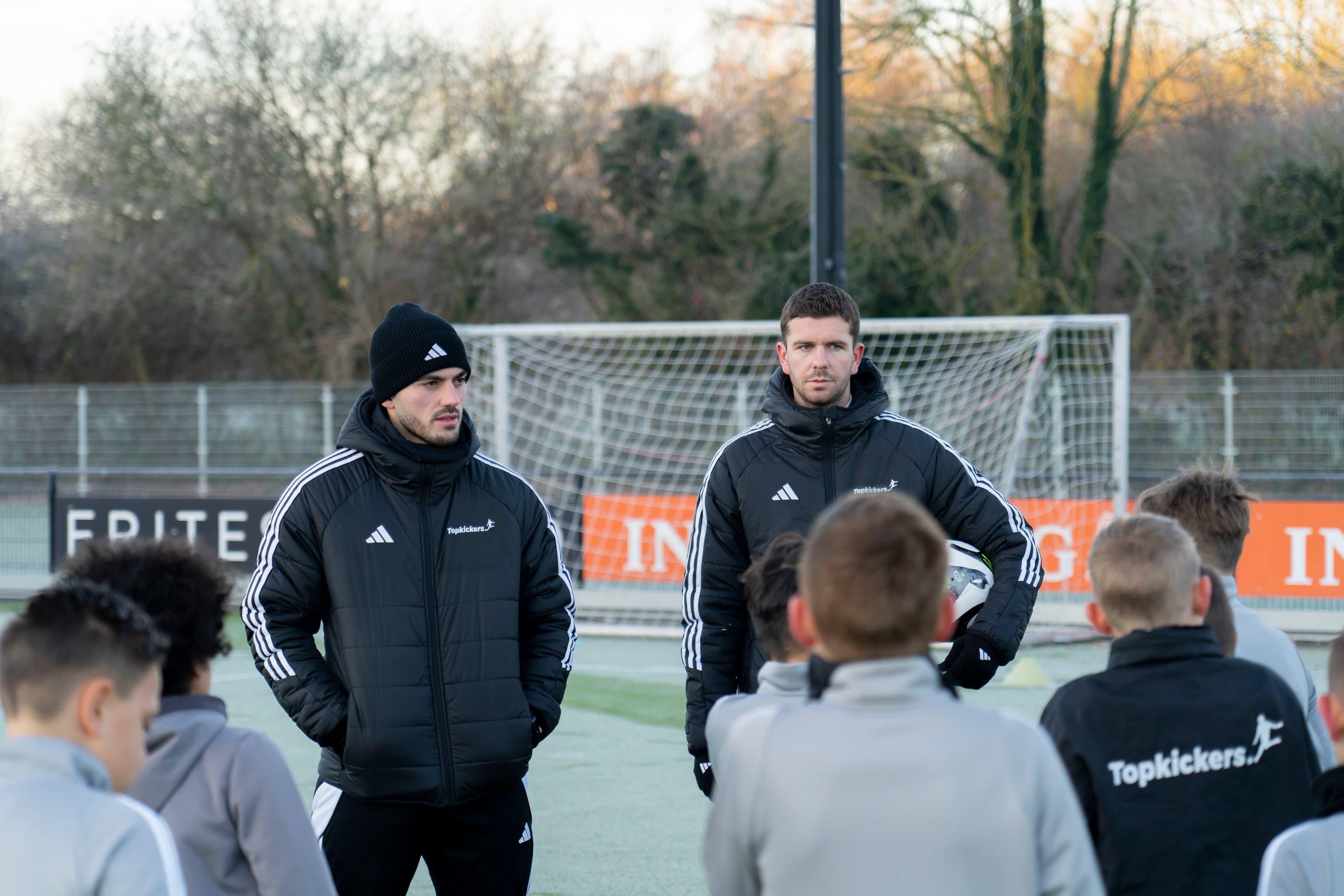 Trainers geven uitleg aan een groep kinderen op het voetbalveld